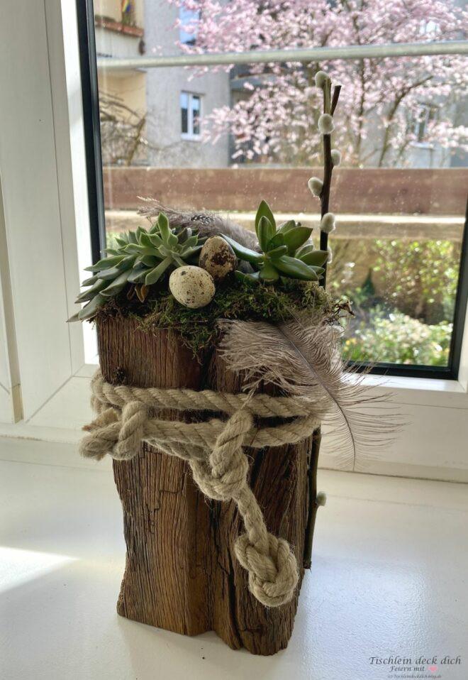 Osterdeko daheim, alter Holzbalken dekoriert mit Moos, Sukkulenten, Wachteleiern und Feder