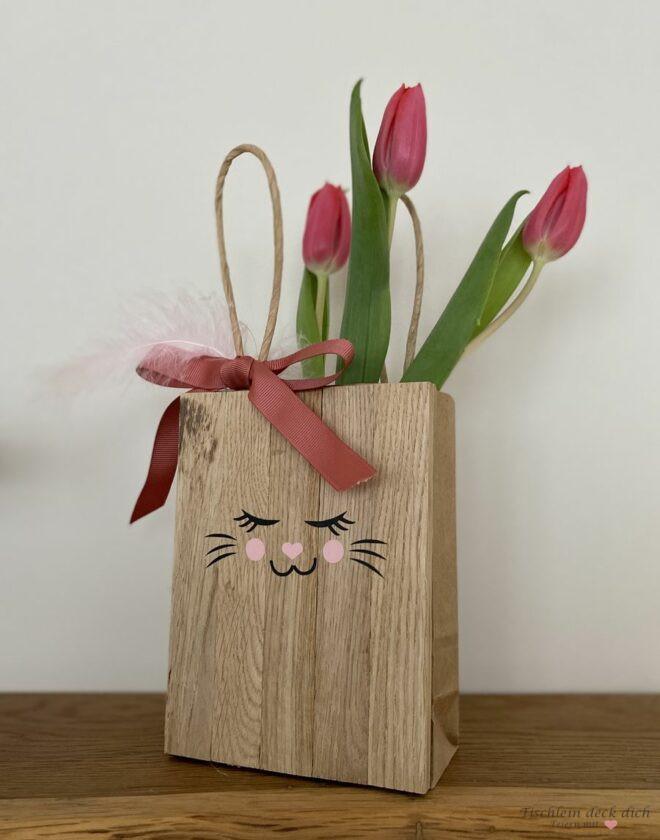 Klötzchentüte mit Osterhasengesicht, roter Schleife und Tulpen