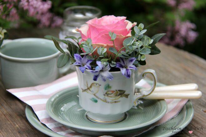 alte Porzellantasse mit Vogelmotiv gefüllt mit Rose und Zweigen