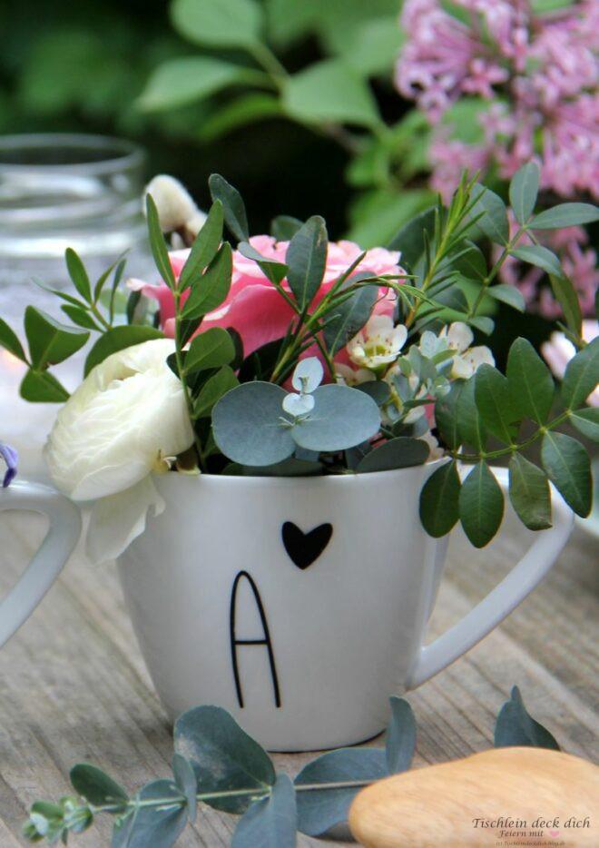 Weiße Porzellantasse gefüllt mit pinkfarbener Rose, weißer Ranunkel und Eukalyptus