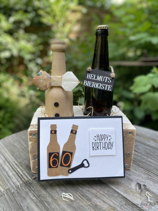 Geldgeschenk zum 60. Geburtstag in einer Holzkiste mit zwei Flaschen, eine Flasche aus Holz, eine aaus Glas und einer Glückwunschkarte zum 60. Geburtstag.