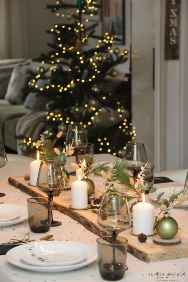 Natürliche weihnachtliche Tischdekoration auf langem Holzbrett mit weißen Kerzen und grünen Weihnachtskugeln