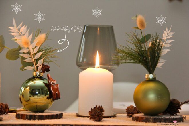 Festliche Weihnachtsdeko auf Holzbrett mit weißen Stumpenkerzen und Vasen aus grünen Weihnachtskugeln