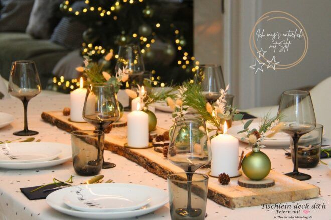 Natürliche Tischdeko zu Weihnachten mit Kerzen, Tannenzweigen und grünen Christbaumkugeln auf einem Holzbrett