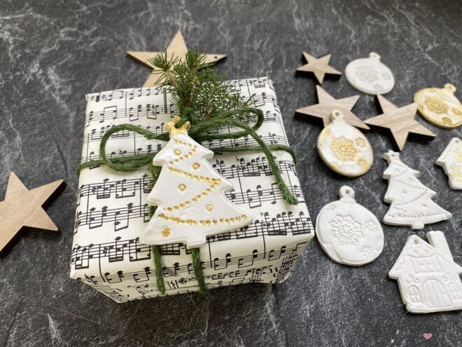 weihnachtliche Geschenkverpackung mit Notenpapier und weiß goldenen Anhängern aus Modelliermasse