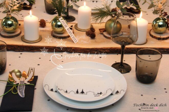 Natürliche Weihnachtstischdeko mit weißen Tellern, schwarzen Gläsern, Kerzen und grünen Kugeln auf Holzbrett